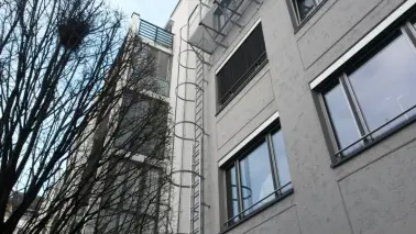 Feuerleiter mit Anschluß an Fluchtbalkon in oberstem Stockwerk bei einem mehrstöckigen Gebäude
