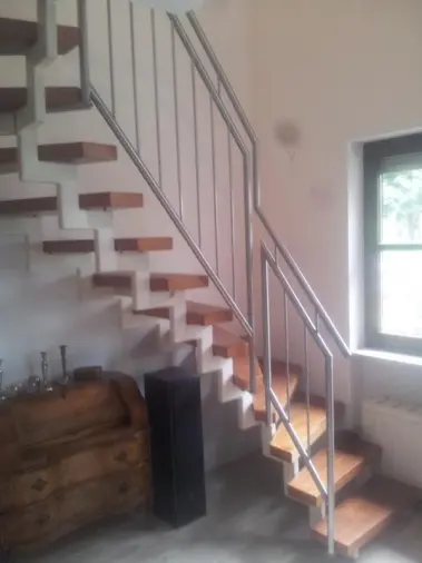 Seitenansicht auf eine Holztreppe mit Edelstahlgeländer, unter der Treppe steht eine Holzkommode